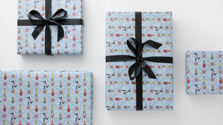 Gift Wrap: Four classic, high-end gift boxes in holiday-themed paper with nutcracker and ballerina motifs, tied with effortless black satin bows, perfect for fun celebrations.
