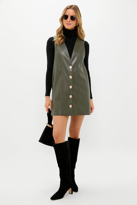 Model in Olive Faux Leather Pinafore Dress over a fitted black turtleneck, styled with suede knee-high boots, gold accessories, and a chic black handbag for an effortless, classic look.