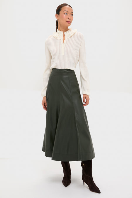 A woman in a molli cream openwork knit blouse, dark green midi leather skirt, and dark brown knee-high boots stands against a plain white background.