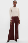 A person in an Altuzarra cream crewneck sweater with delicate beadwork, burgundy satin wide-leg pants, and dark pointed-toe heels stands against a plain background.