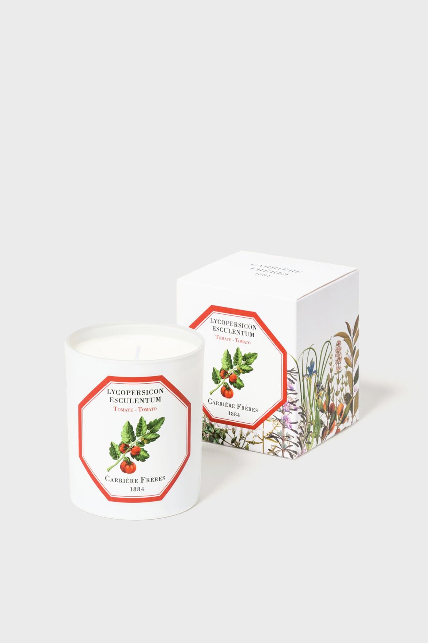 A white luxury Carrière Frères candle, crafted from vegetable wax in a glass jar with a botanical tomato label, sits beside its matching floral-illustrated box.