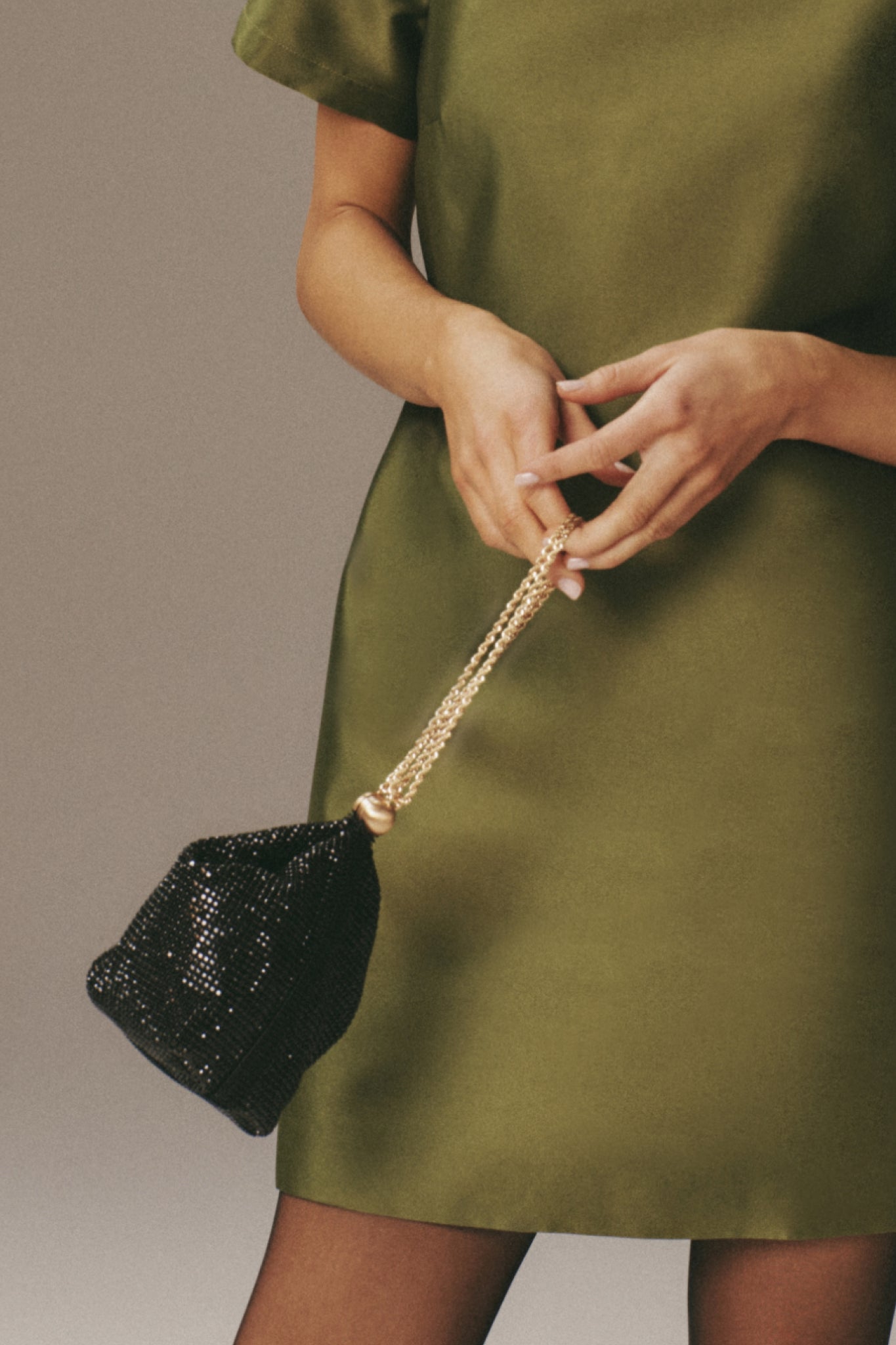Classic Black Rue Wristlet adorned with black beads and a gold chain, held by a model in an olive satin dress, exuding effortless, high-end style.
