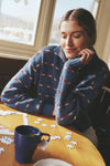 Young woman in a classic Navy Striped Jansen V-Neck Polo Sweater, thoughtfully assembling a puzzle at a café table, embodying effortless and high-end style.