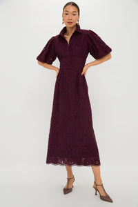 A woman wears a Tuckernuck burgundy eyelet dress with puff sleeves, a collared neckline, and brown low-heeled shoes.