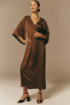 Woman in a classic, effortless Chocolate Brown Satin Emiliana Maxi Dress with kimono sleeves, holding a clutch and wearing block-heel sandals, embodying high-end, fun elegance.
