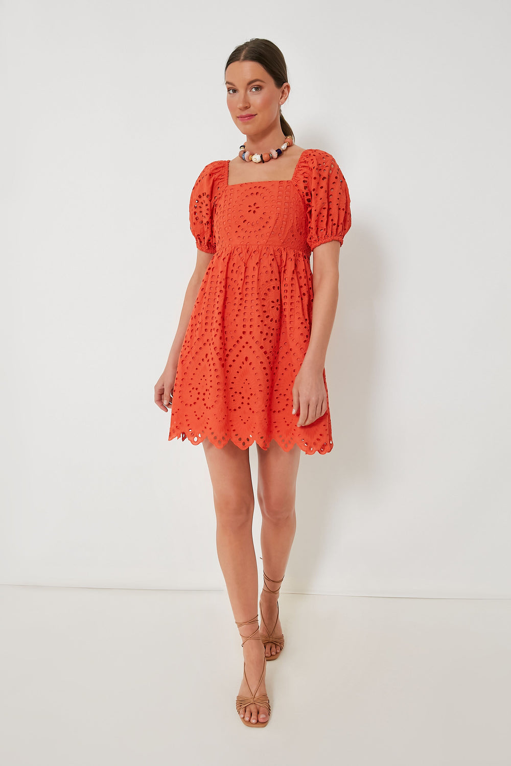 A woman wears a red Hyacinth House Clara Dress, featuring puff sleeves in an eyelet mini dress style.
