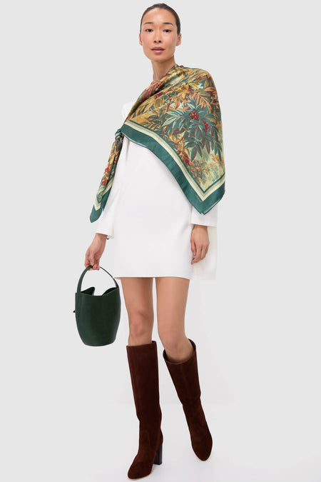 Woman in a white dress wearing classic, effortless Espresso Suede Goldy Boots; knee-high, chunky-heeled, paired with a chic botanical shawl and dark green handbag.