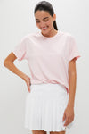 A woman styled in Tnuck Sport’s light pink SPF crewneck tee and white pleated skirt looks down, her hair tied in a ponytail.