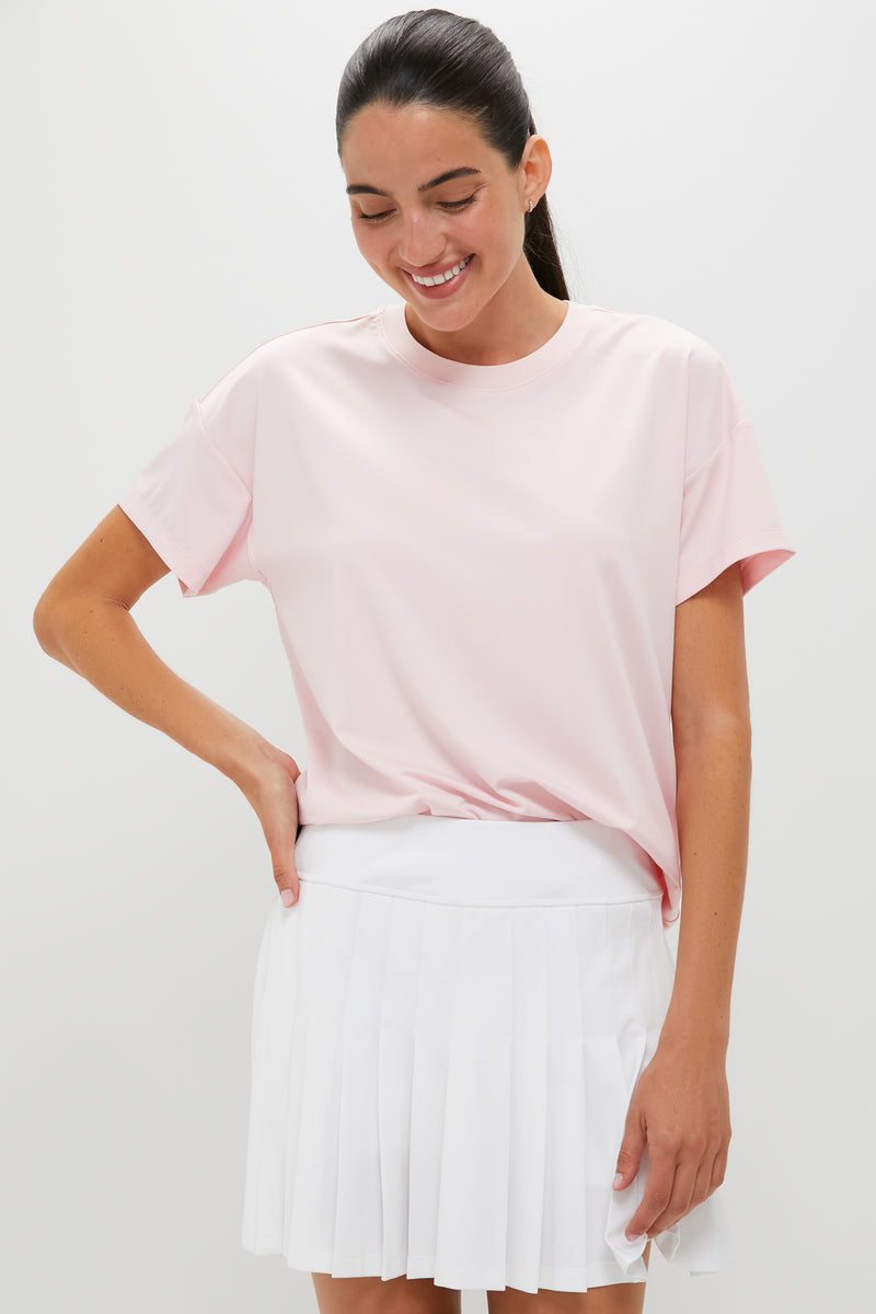 A woman styled in Tnuck Sport’s light pink SPF crewneck tee and white pleated skirt looks down, her hair tied in a ponytail.