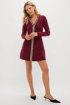 A woman models a Hyacinth House burgundy knit mini dress with a fit-and-flare silhouette and white lace trim, paired with black pointed-toe heels, against a plain background.