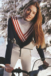 Young woman on snowmobile wearing Chevron Johnny Turtleneck Sweater, a classic, retro, semi-fitted knit, evoking effortless high-end style in a fun, snowy winter setting.