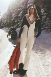 Young woman in Snow White JG Bib Ski Pant, holding a red jacket on a snowy trail, showcasing classic, high-end, and effortless style with fun, functional features.