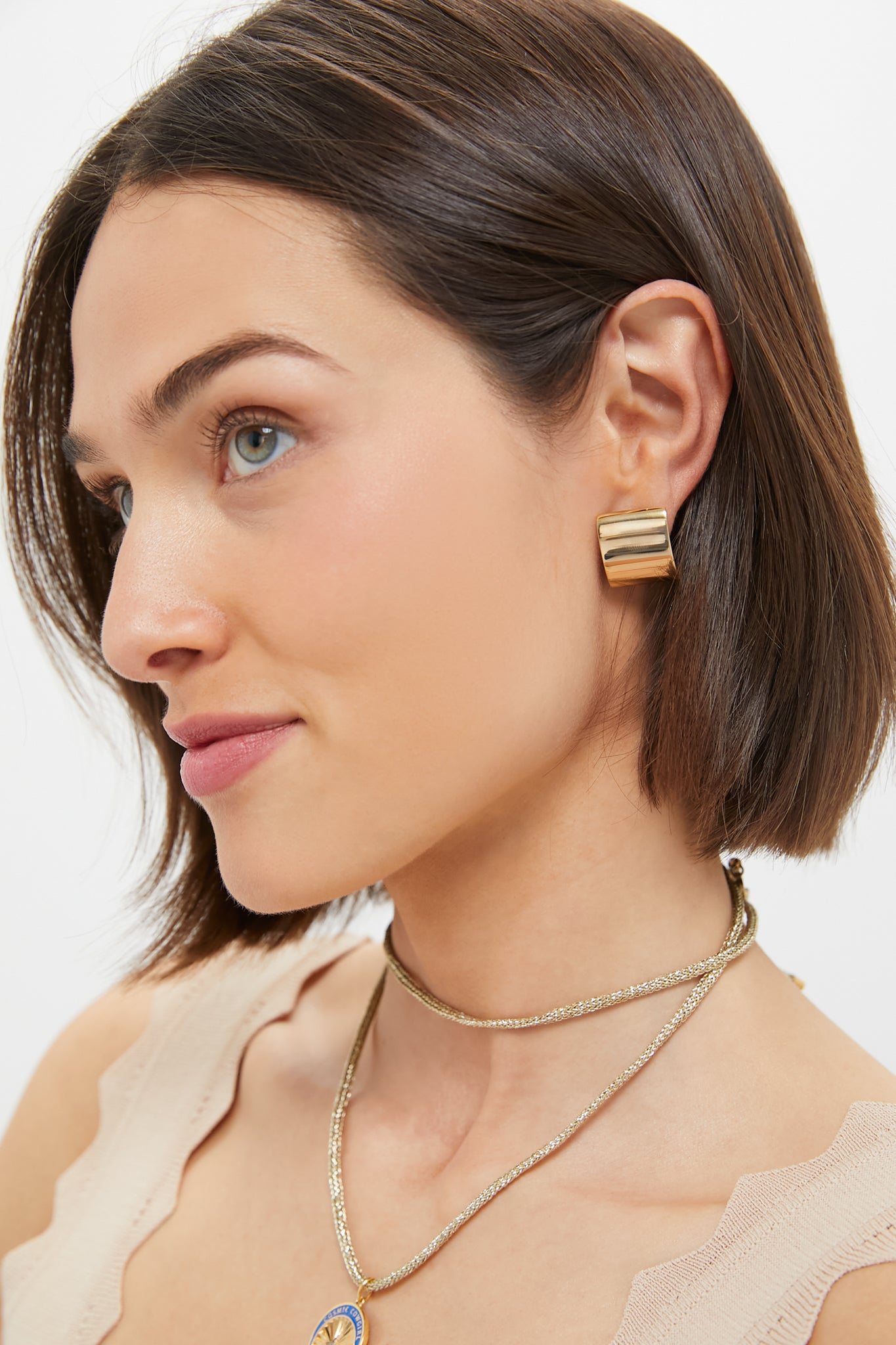 A woman with short brown hair wears Lie Studio gold-plated sterling silver earrings, a beige top, and layered gold necklaces, shown in profile against a white background.