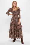 Woman models an effortless, high-end look with a classic, brown floral dress, accessorized by the Gold Lucky Feather Pendant, adding whimsical elegance and fun to her ensemble.