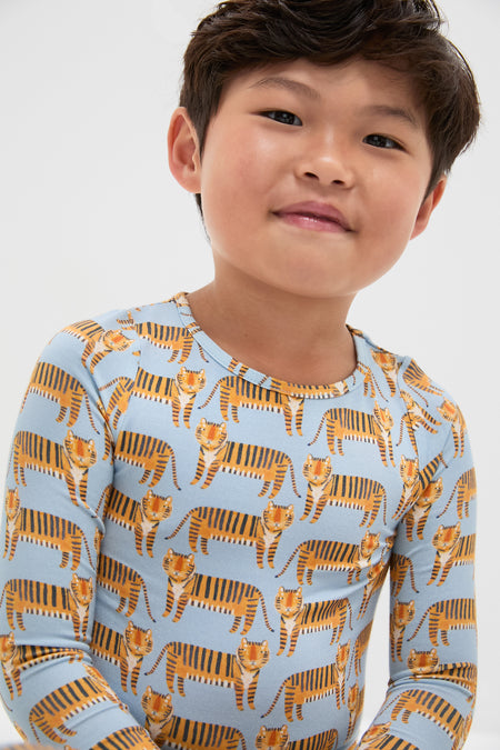 Child wearing Tigers Kids Bamboo Pj Set, featuring a fun cartoon-tiger motif on a classic light-blue top. The effortlessly cool set is soft, breathable, and high-end.