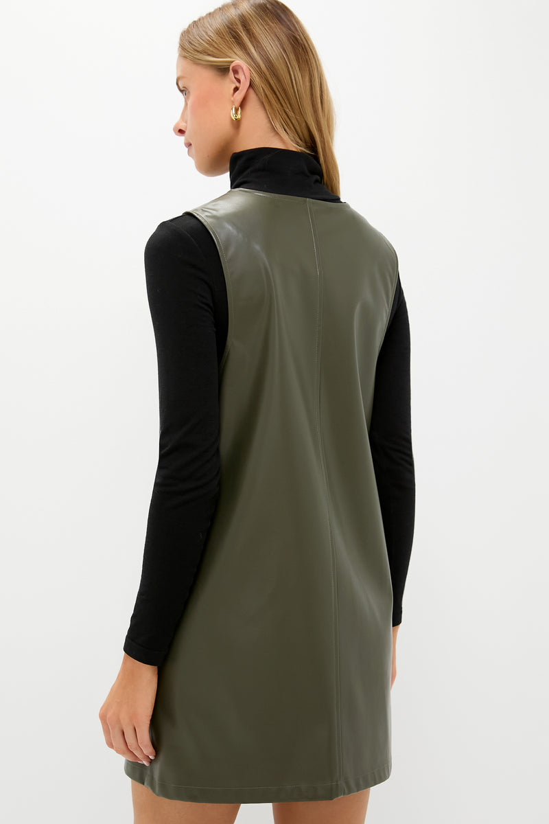 Woman in an olive faux leather pinafore dress over a black turtleneck, embodying a classic, effortless style with a single gold hoop earring.
