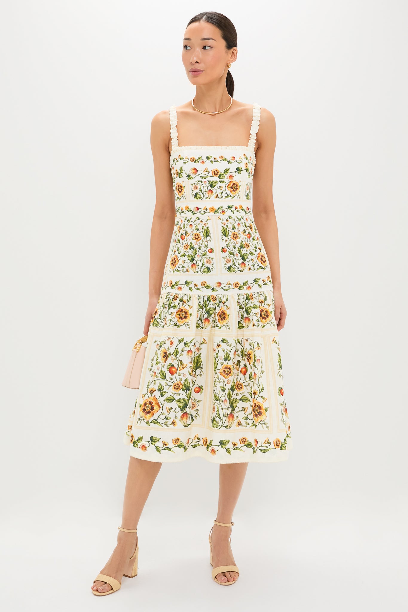 Model wears the classic Uchuva Nispero Midi Dress, featuring an effortless square neckline and ruffled straps, paired with a fun blush-pink handbag and high-end beige sandals.