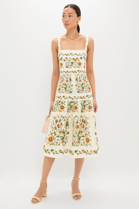 Model wears the classic Uchuva Nispero Midi Dress, featuring an effortless square neckline and ruffled straps, paired with a fun blush-pink handbag and high-end beige sandals.