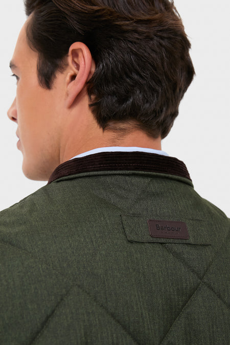 Man wearing Olive Winter Finn Gilet with diamond-quilted texture, brown corduroy collar, and Barbour leather patch, showcasing classic, effortless, high-end style for unpredictable weather.