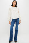 Woman models Ivory Patchwork Embroidered Cressida Blouse with intricate lace yoke and sleeves, paired with flared jeans and dark-brown ankle boots for a classic, effortless look.