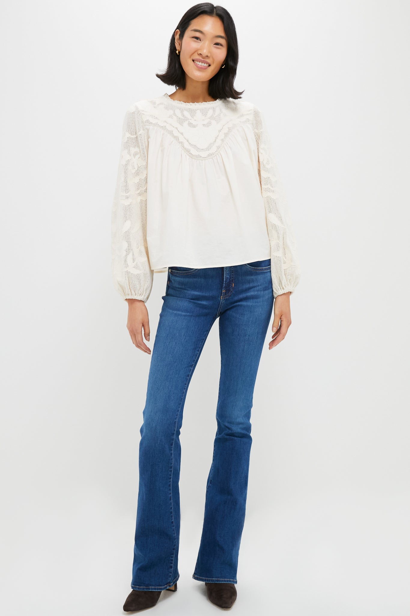 Woman models Ivory Patchwork Embroidered Cressida Blouse with intricate lace yoke and sleeves, paired with flared jeans and dark-brown ankle boots for a classic, effortless look.