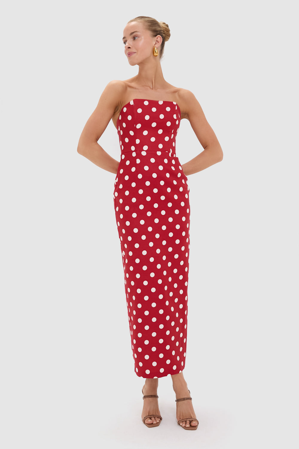 A person stands wearing POSSE’s strapless, ankle-length red polka dot dress with white spots and beige heeled sandals—an ideal occasion dress.