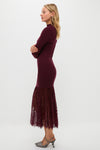 A woman in profile wears a Hyacinth House Suzanne dress—a long-sleeved, burgundy knit evening dress with a lace hem—paired with gray heels, posing against a plain white background.