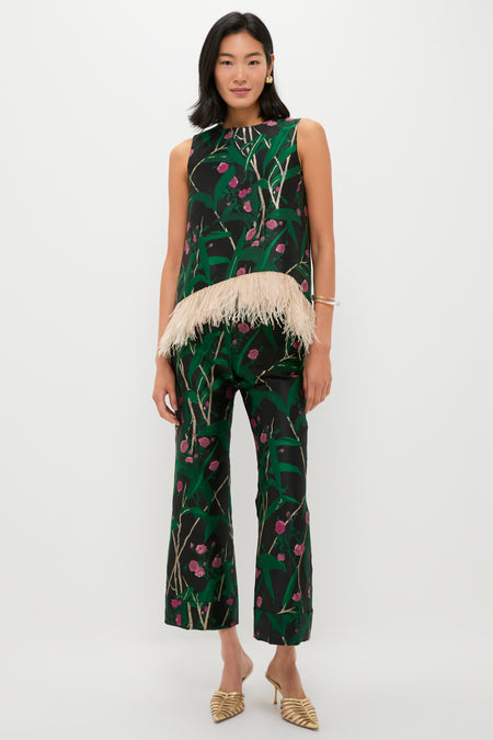 A woman stands against a white background wearing a La DoubleJ sleeveless black top with green and pink floral print and beige feather trim, paired with Hendrix Pants and beige pointed-toe shoes.