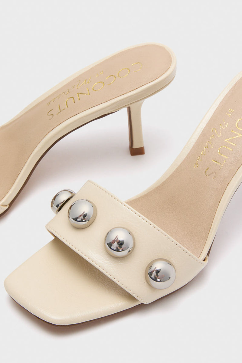 Matisse cream heeled mules feature open toes, square fronts, and wide front straps adorned with metallic round studs.