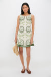 Model in Ireland Green Layla Mini Dress with botanical motifs, holding a straw hat. Effortless, classic A-line style, perfect for fun outdoor events; embodies high-end Tuckernuck charm.
