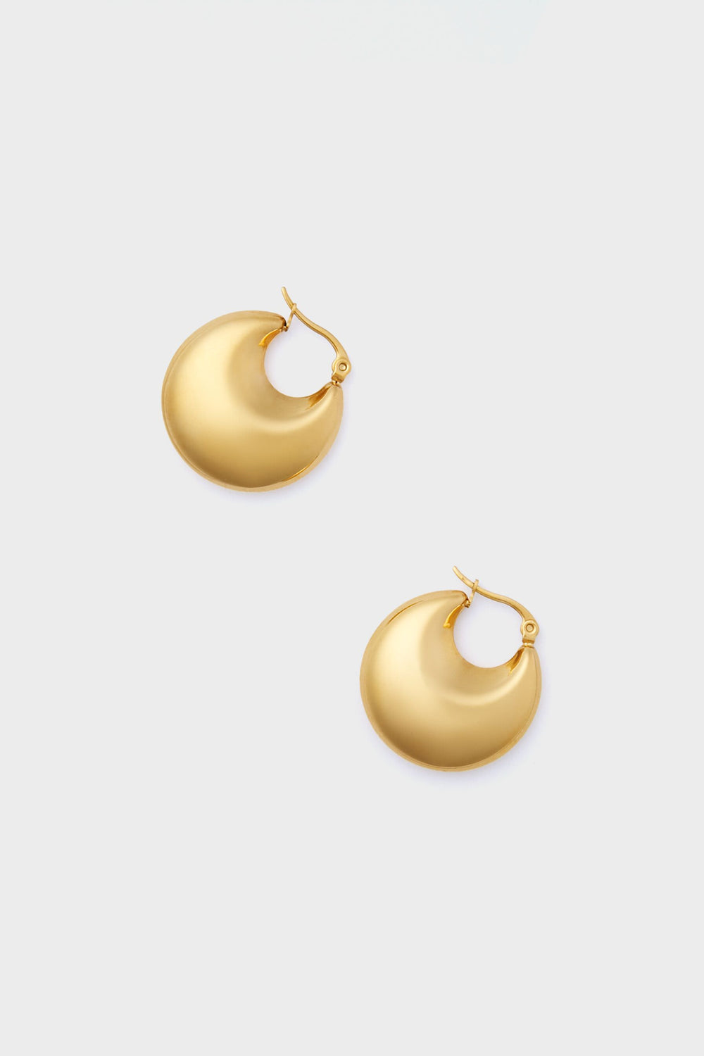 The Gold Lara Earrings by Petit Moments are chunky, round gold hoops with a latch back closure, crafted by a female-owned brand to add effortless elegance to any look.