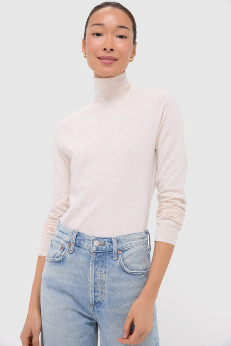 A person wears a Nude Lucy cream turtleneck and light blue high-waisted jeans, effortlessly showcasing style in a Nude Lucy light beige merino wool sweater.