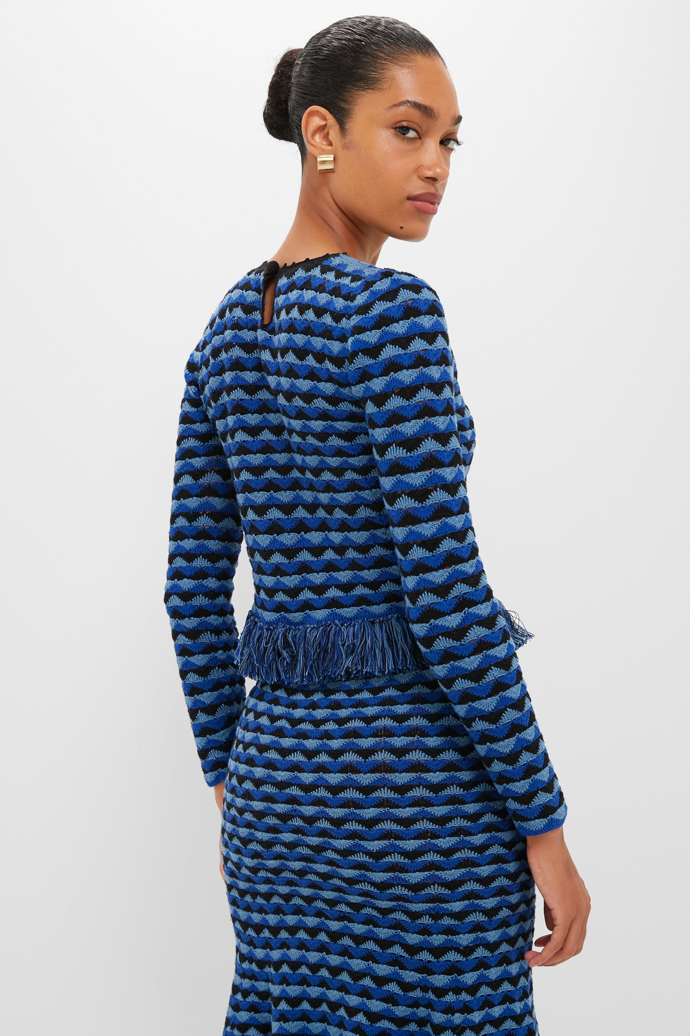 Woman models the Blue and Black Profundo Long Sleeve Top, showcasing its classic wave-like stripes and fringe hem, capturing an effortless and high-end style.