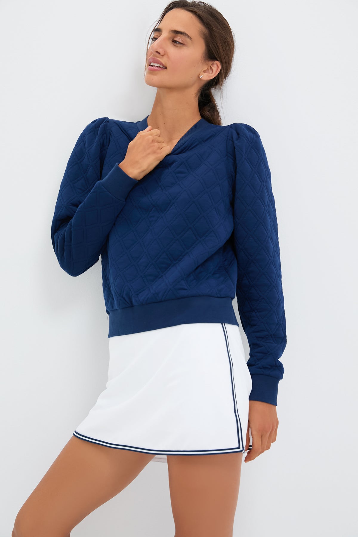 A woman wears the Tnuck Sport Puff Sleeve Campbell Pullover in navy diamond quilting and a white skirt with navy piping, highlighting her stylish look.