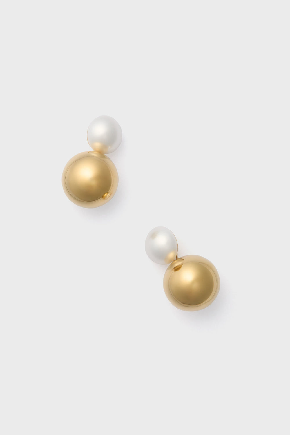 A pair of Gold Pearl Sphere Earrings by Petit Moments, featuring a small white pearl above a larger metallic gold sphere, crafted by a female-owned jewelry brand.