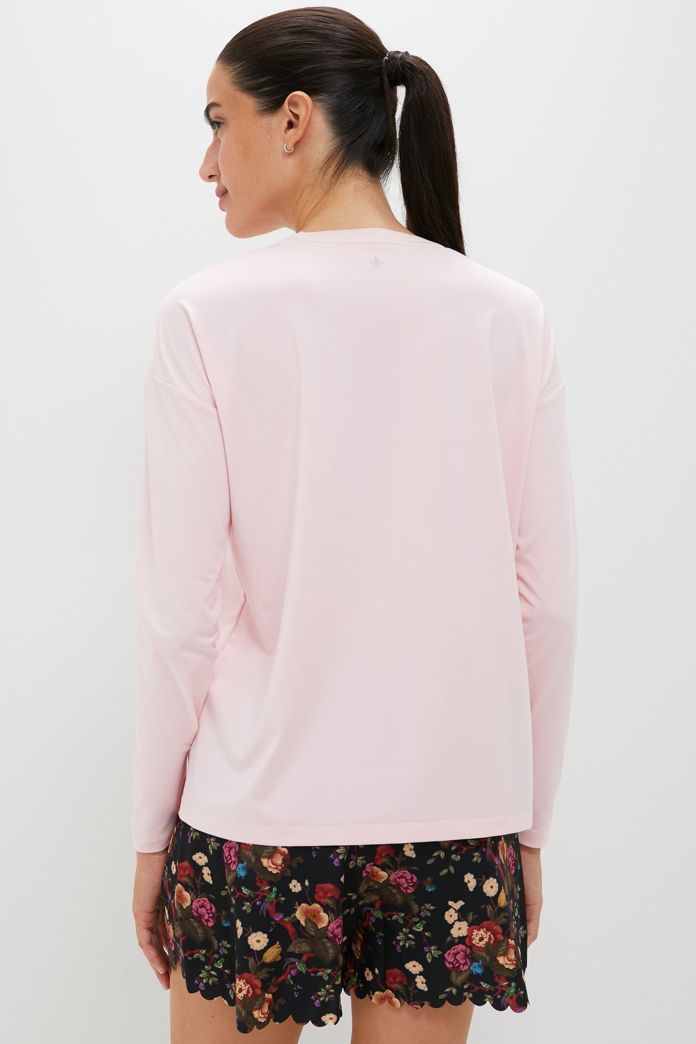 Back view of a woman in a classic, effortless Pink Long Sleeve Performance Jersey Ryan Boyfriend Tee, paired with floral-patterned shorts, embodying fun and high-end style.