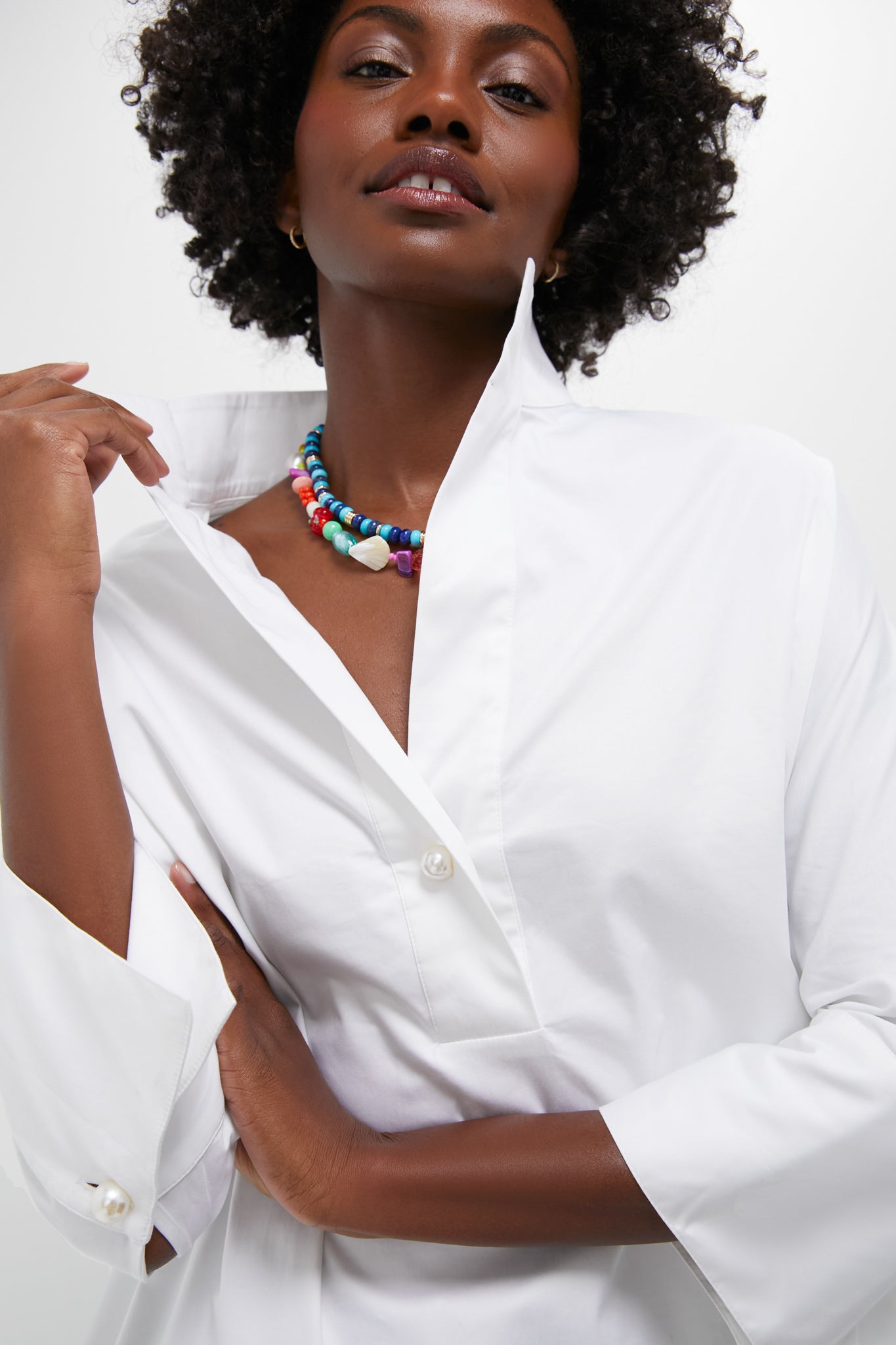 A person in a Tuckernuck Blanc Willow Blouse with a button-front half-placket and popped collar, paired with a colorful beaded necklace.