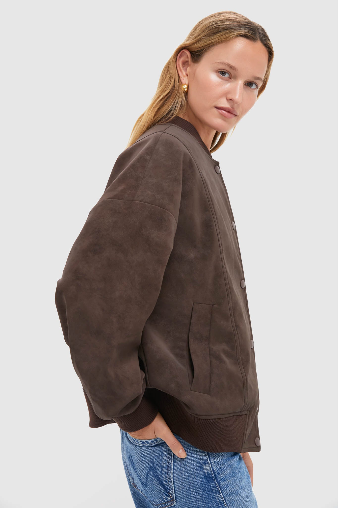 Woman wearing the Chocolate Alfie Jacket, a classic, high-end faux leather bomber with ribbed trims and snap buttons, styled effortlessly with light-wash jeans.