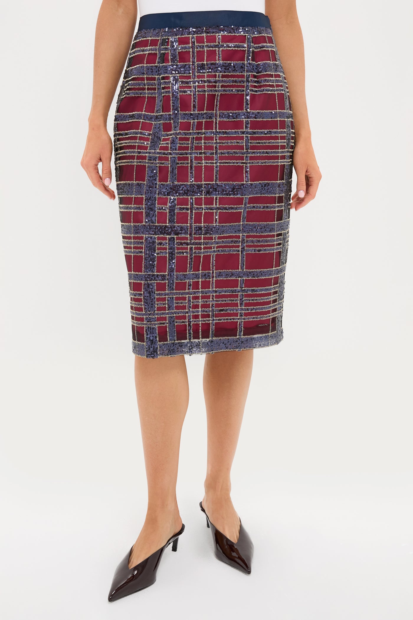 A person wearing a Tuckernuck knee-length pencil skirt in red and navy plaid, perfect for holiday parties, paired with black pointed-toe shoes.
