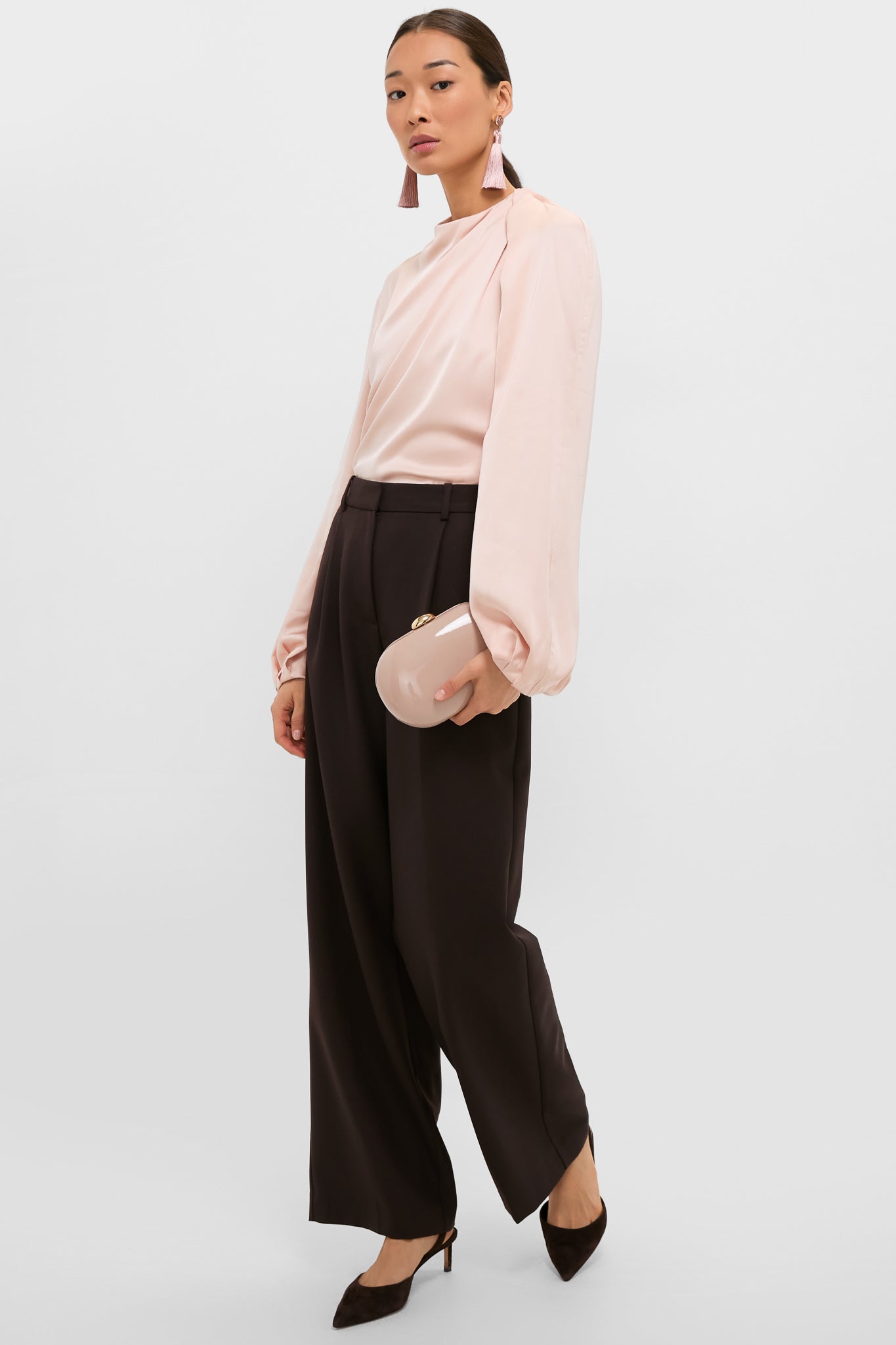 Model showcasing an effortless, high-end look with a Latte Patent Selena Clutch Bag, styled with classic, wide-leg trousers and a satin blouse for a fun, confident ensemble.