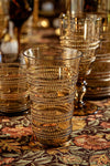 Amber Ella Large Tumbler with classic spiral design, mouth-blown, effortlessly combines fun and high-end style, set on an autumnal floral tablecloth with similar textured glassware behind.