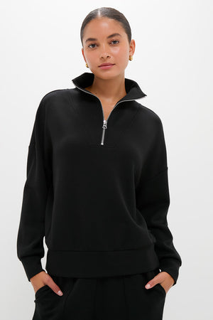 A woman models modern athleisure style in a black Varley half zip sweater, hands in pockets.
