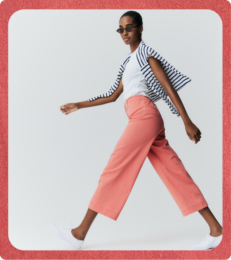 Woman walking in a white tee and red pants with a blue and white striped tee over her shoulders. 
