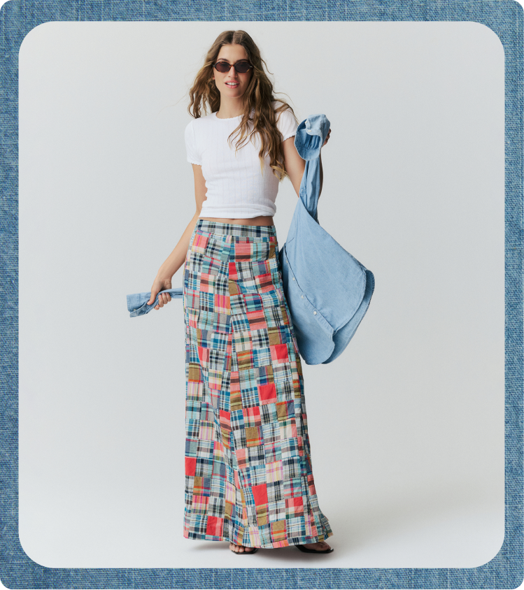 Woman in a white tee with a madras maxi skirt holding a chambray shirt behind her. 