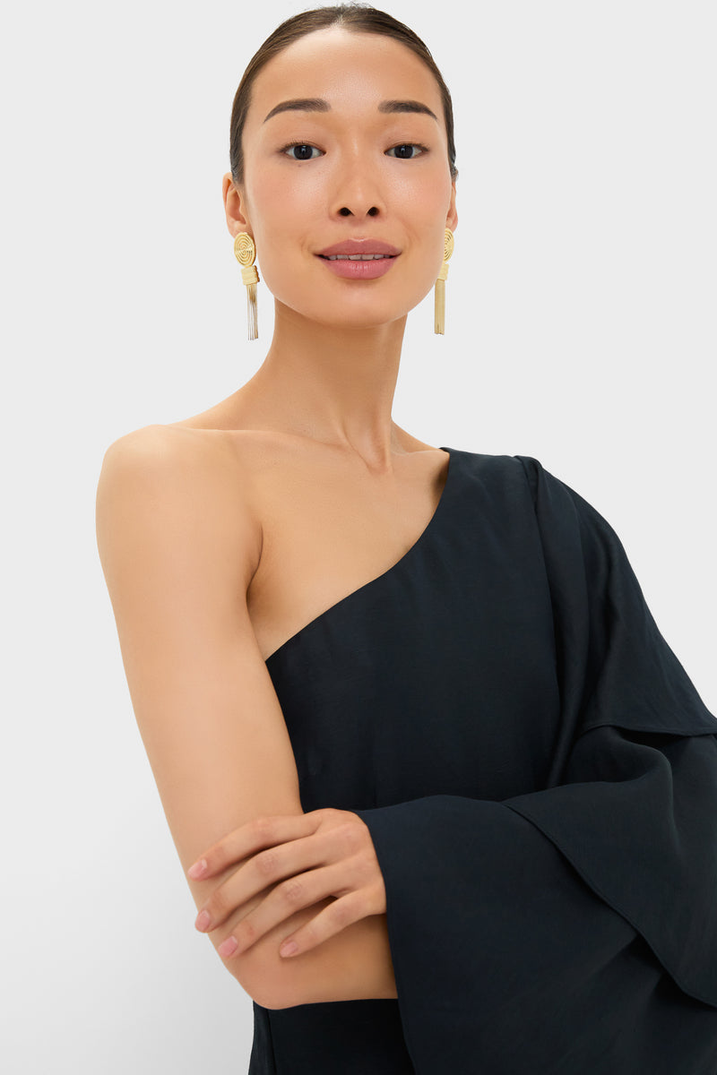 Woman in Black Bidi Bidi Bom Bom Tea Length Dress with asymmetric neckline, dramatic ruffled sleeve, and statement earrings, embodying classic elegance and effortless, high-end style.