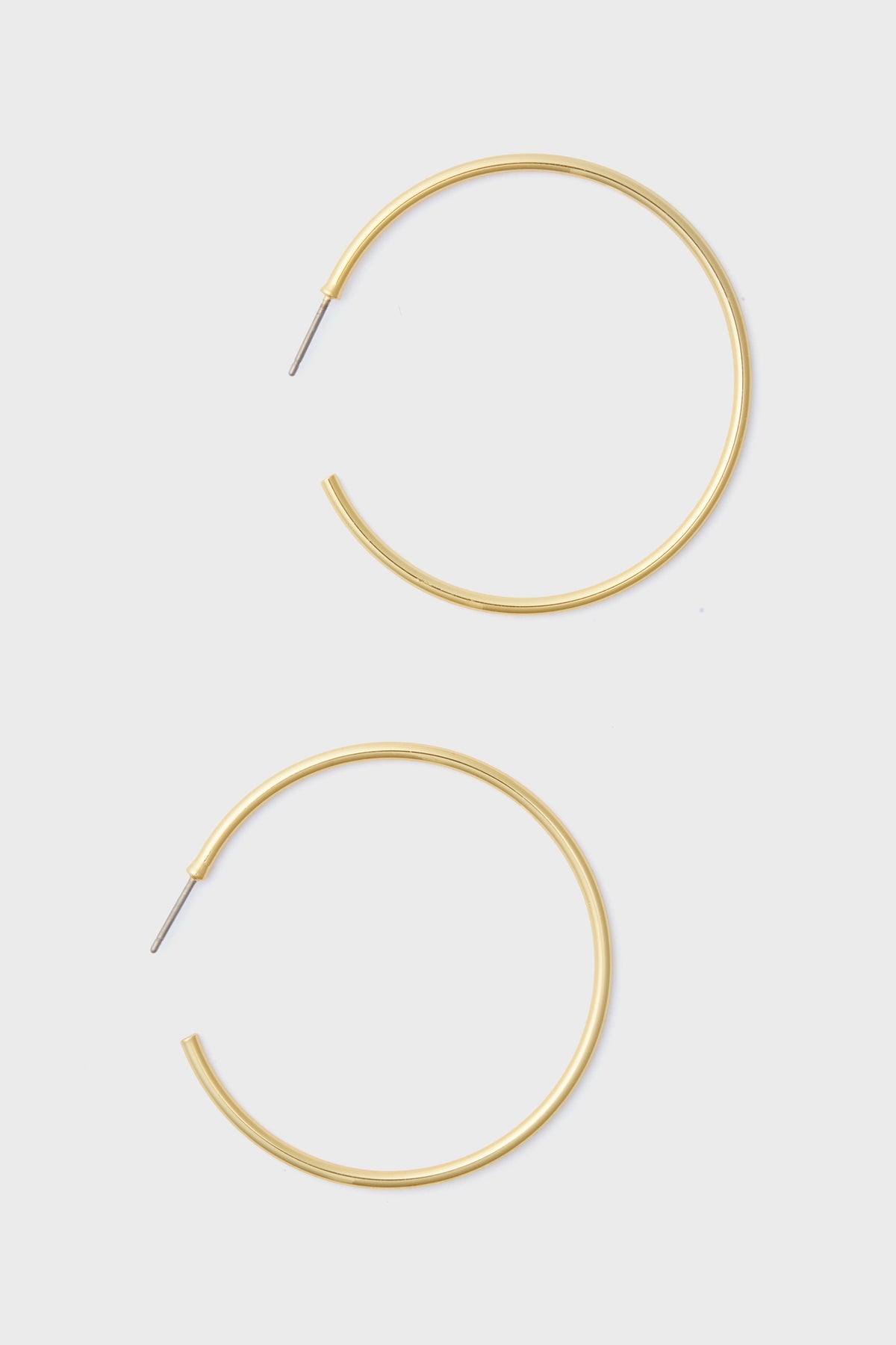 A pair of large, thin 14k gold plated hoop earrings with straight posts from Tuckernuck Jewelry—perfect hypoallergenic earrings for everyday style.