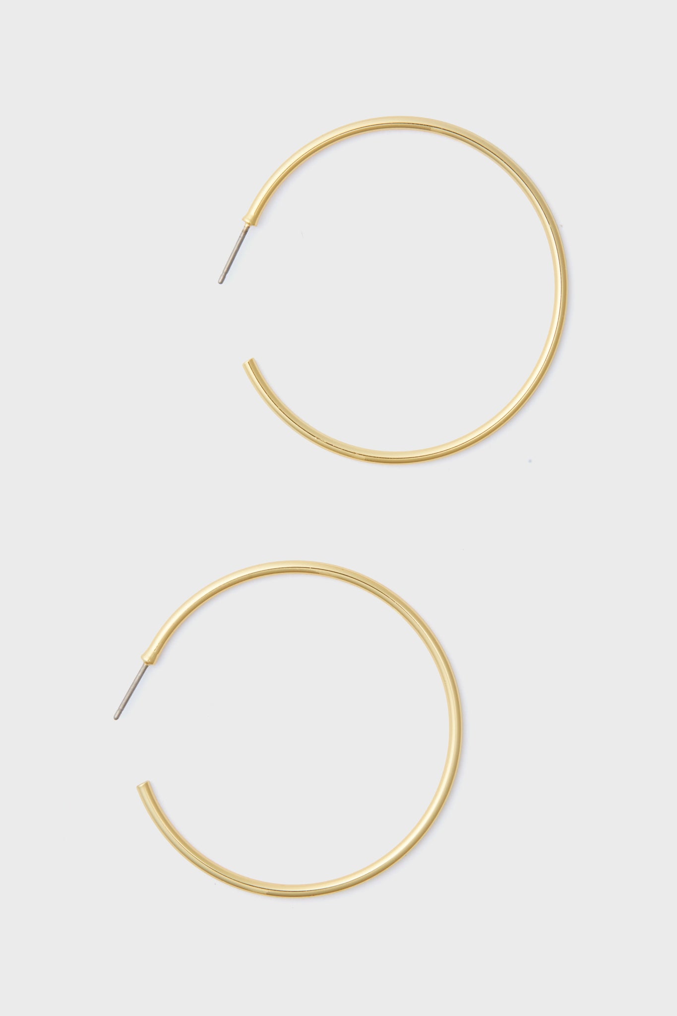 A pair of large, thin 14k gold plated hoop earrings with straight posts from Tuckernuck Jewelry—perfect hypoallergenic earrings for everyday style.