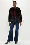 A woman poses against a plain background in a Vanessa Bruno dark faux fur jacket, maroon top, blue wide-leg jeans, and pointed-toe heels—ideal for sophisticated winter layering.
