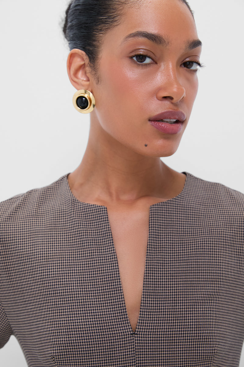 Woman wearing Onyx Alva Earrings, a classic, high-end accessory with an oversized gold design and black center, paired with a micro-houndstooth top. Effortlessly fun and stylish.