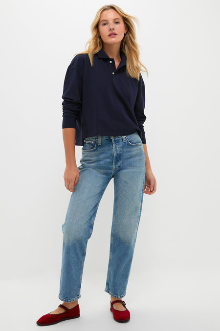 Woman models the Navy Long Sleeve Pique Holmes Boyfriend Polo with a classic, effortless style, showcasing its boxy silhouette and textured fabric, paired with light jeans and red flats.